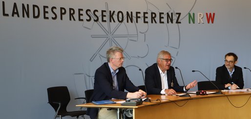Pressekonferenz mit drei Personen am Tisch